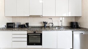 A modern kitchen with white cabinets, a built-in oven, a dishwasher, a microwave, a coffee maker, and a kettle. - GuestReady - Apartment near beach retreat (Vila do Conde)