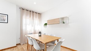 A modern dining area with a wooden table, white chairs, a small plant on a shelf, and a framed picture on the wall. - GuestReady - Apartment near beach retreat (Vila do Conde)