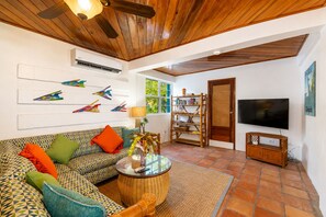 A living room with a patterned sofa, a glass coffee table, a television, and a bookshelf. - Villa Stella Di Mare - 4 Bedroom Luxurious Beachfront & Pool Villa (San Pedro)