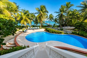 A swimming pool with a curved edge, surrounded by palm trees and lounge chairs. - Villa Stella Di Mare - 4 Bedroom Luxurious Beachfront & Pool Villa (San Pedro)