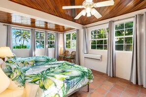 A room with two beds, a ceiling fan, large windows with curtains, a table with chairs, and an air conditioning unit. - Villa Stella Di Mare - 4 Bedroom Luxurious Beachfront & Pool Villa (San Pedro)