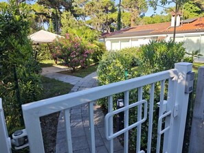 A gated entrance to a property with a pathway leading to a house. - Villa LANTERNA - Lignano Sabbiadoro (Lignano Sabbiadoro)