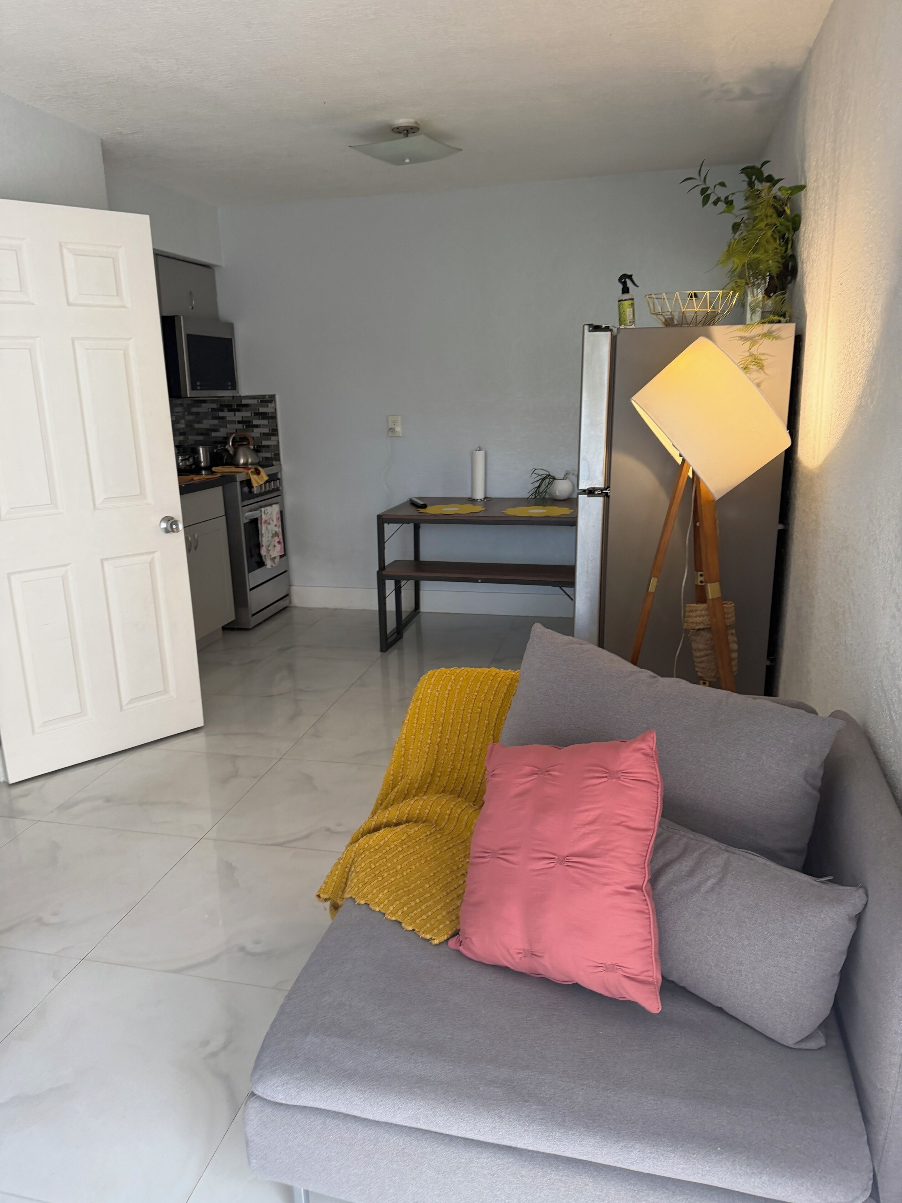 A living room with a sofa, a lamp, and a kitchen in the background.. Charming apartment in fantastic Oakland Park with cool AC - Pets OK ! huge yard
