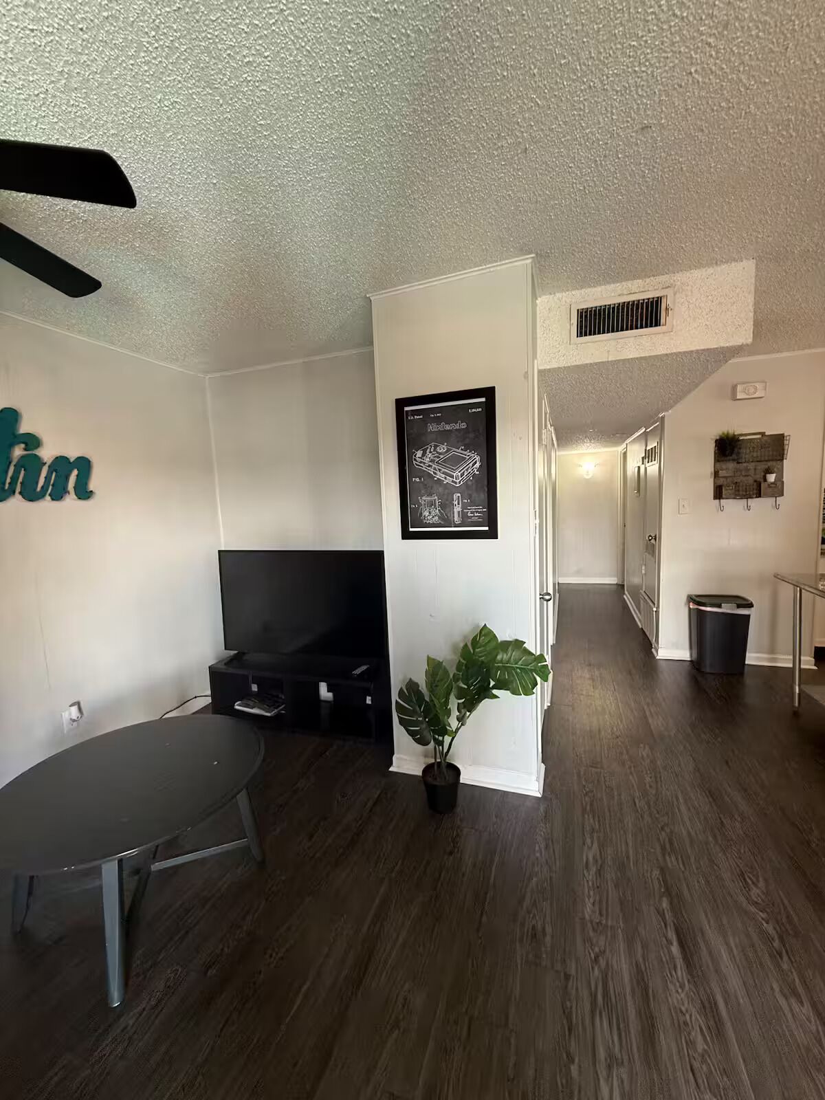 Habitación con televisión de pantalla plana, una planta en maceta, ventilador de techo y un permiso patentado de Nintendo enmarcado.