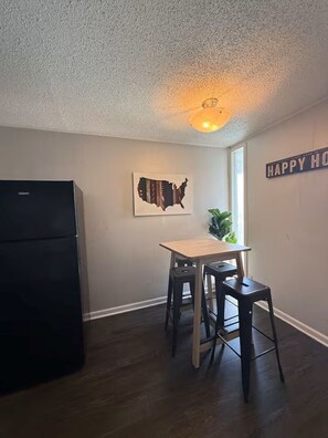 A kitchen with a refrigerator, a wooden table, two stools, a wall-mounted map, and a 'HAPPY HOME' sign. - Great 2x1 apt by West Campus! (Austin)