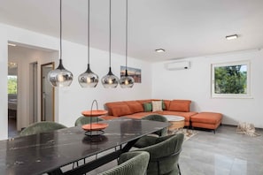 A modern interior with a dining table, chairs, a sofa, and pendant lights.