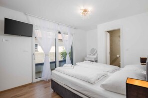 A bedroom with a bed, a TV mounted on the wall, a bedside table with a mirror, and a door leading to a bathroom.