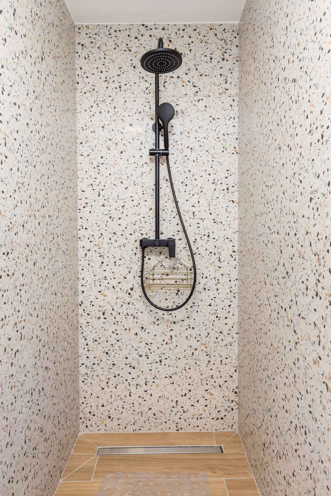 Eine Dusche mit Handbrause und Regendusche, vor einer Wand mit Farbflecken.