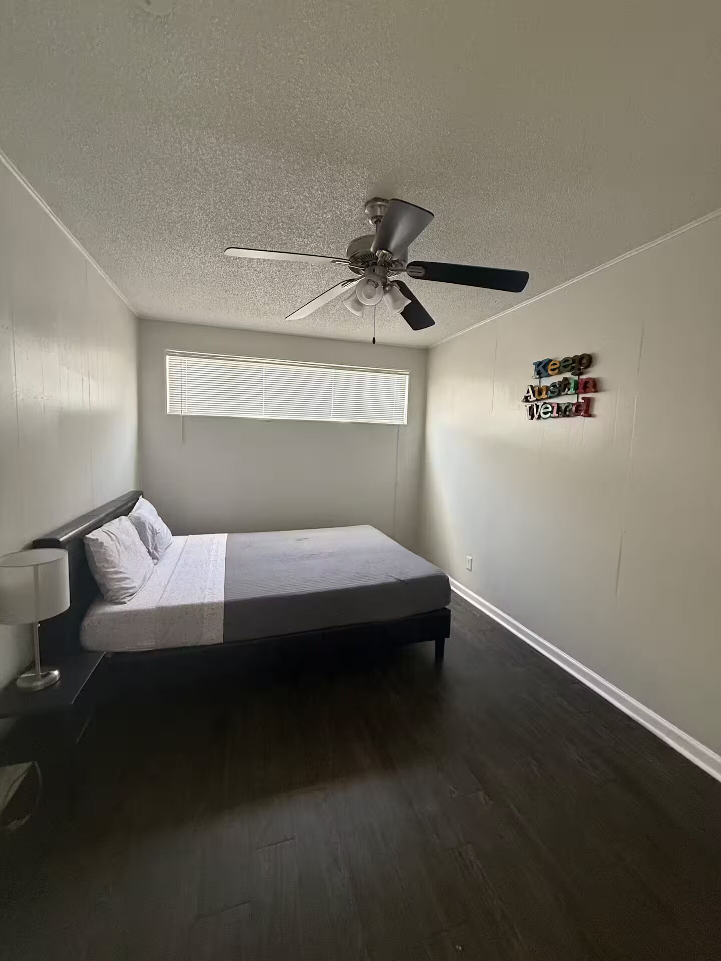 A bedroom with a bed, a ceiling fan, a window with blinds, and a wall decoration.