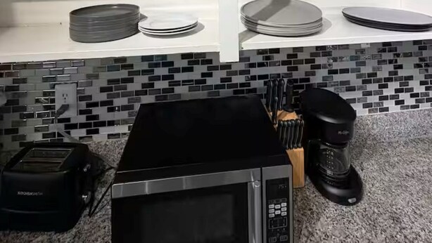 A kitchen with white shelves, a microwave, a toaster, and a coffee maker. - Radiant 2x1 apt by West Campus UT! (Austin)