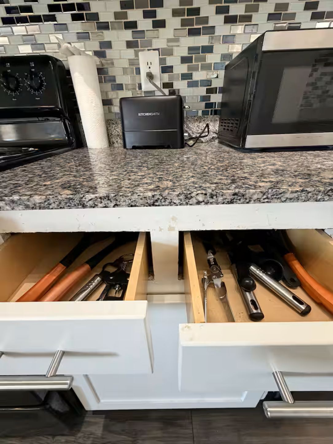 A kitchen with a granite countertop, a built-in microwave, and a kettle.