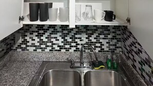 A kitchen with a double sink, white cabinets, and a tiled backsplash. - Radiant 2x1 apt by West Campus UT! (Austin)