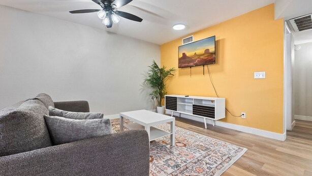 Un soggiorno con un divano, un tavolino, un mobile TV, una ventola a soffitto e un quadro appeso al muro.