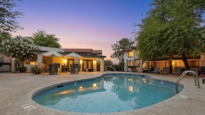 Une piscine avec une terrasse carrelée, un patio couvert avec des chaises et un bâtiment doté d’un toit rouge.