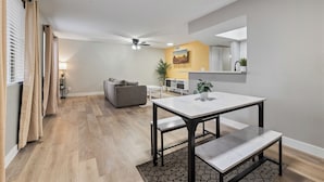 A modern living room with a sofa, a dining table with benches, a ceiling fan, and a kitchen area in the background. - Great for Mid/Long Stays - Pool - King Bed (Mesa)