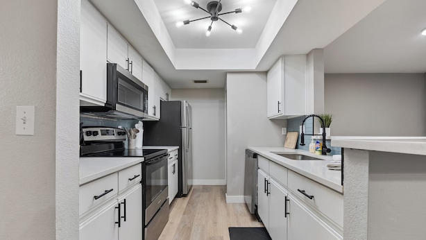Une cuisine moderne avec des meubles blancs, un réfrigérateur noir, une cuisinière et un luminaire au plafond.