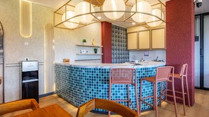 A modern kitchen with a blue tiled island, wooden chairs, and pendant lighting. - Cove Meraya (Tibubeneng)