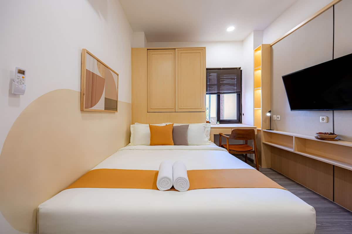 A hotel room with a bed, a desk, a television, and a window.