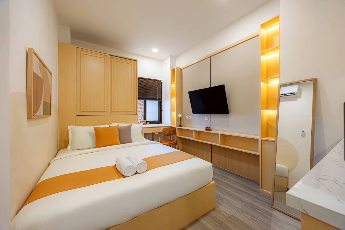 A modern hotel room with a large bed, a desk, a TV, and a mirror.