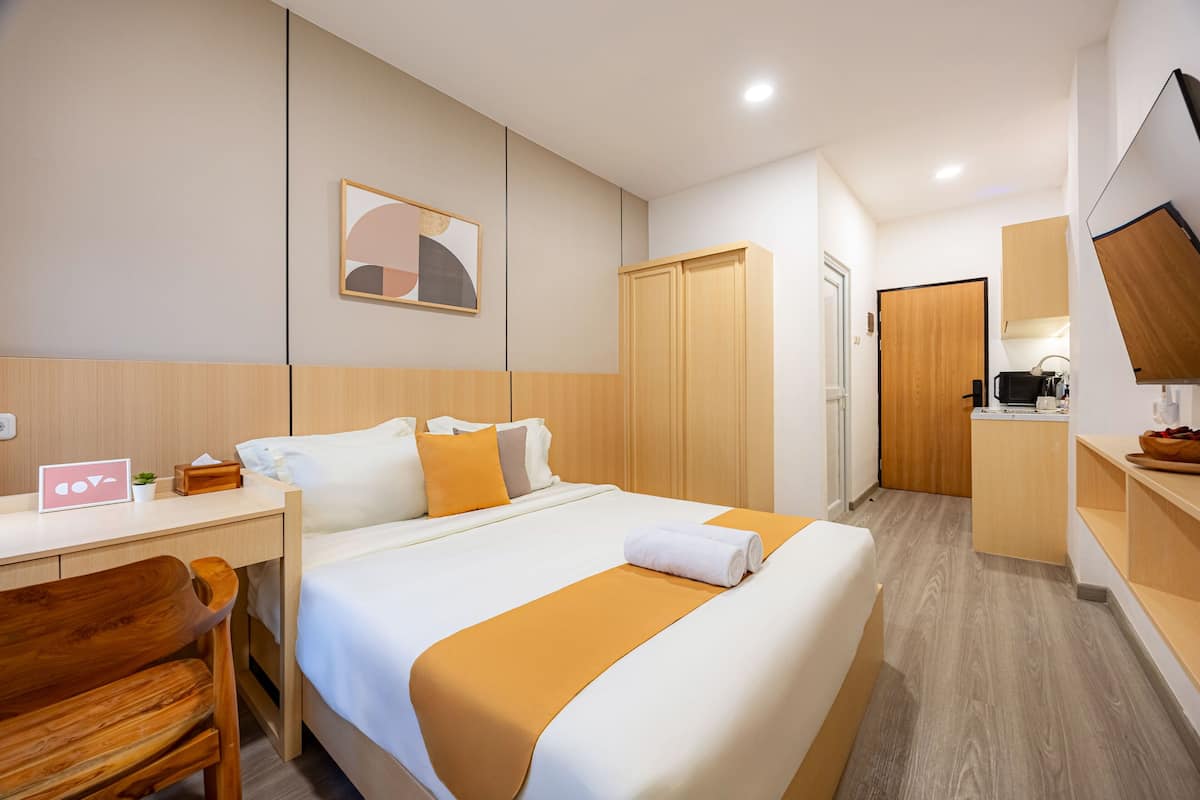 A hotel room with a bed, a desk, a chair, a wardrobe, a mirror, and a kitchenette.