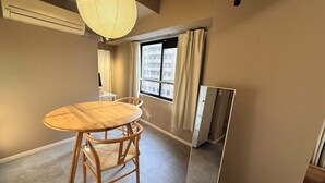Ein Zimmer mit einem runden Holztisch, zwei Stühlen, einem großen Spiegel, einem Fenster mit Vorhängen und einer Klimaanlage.