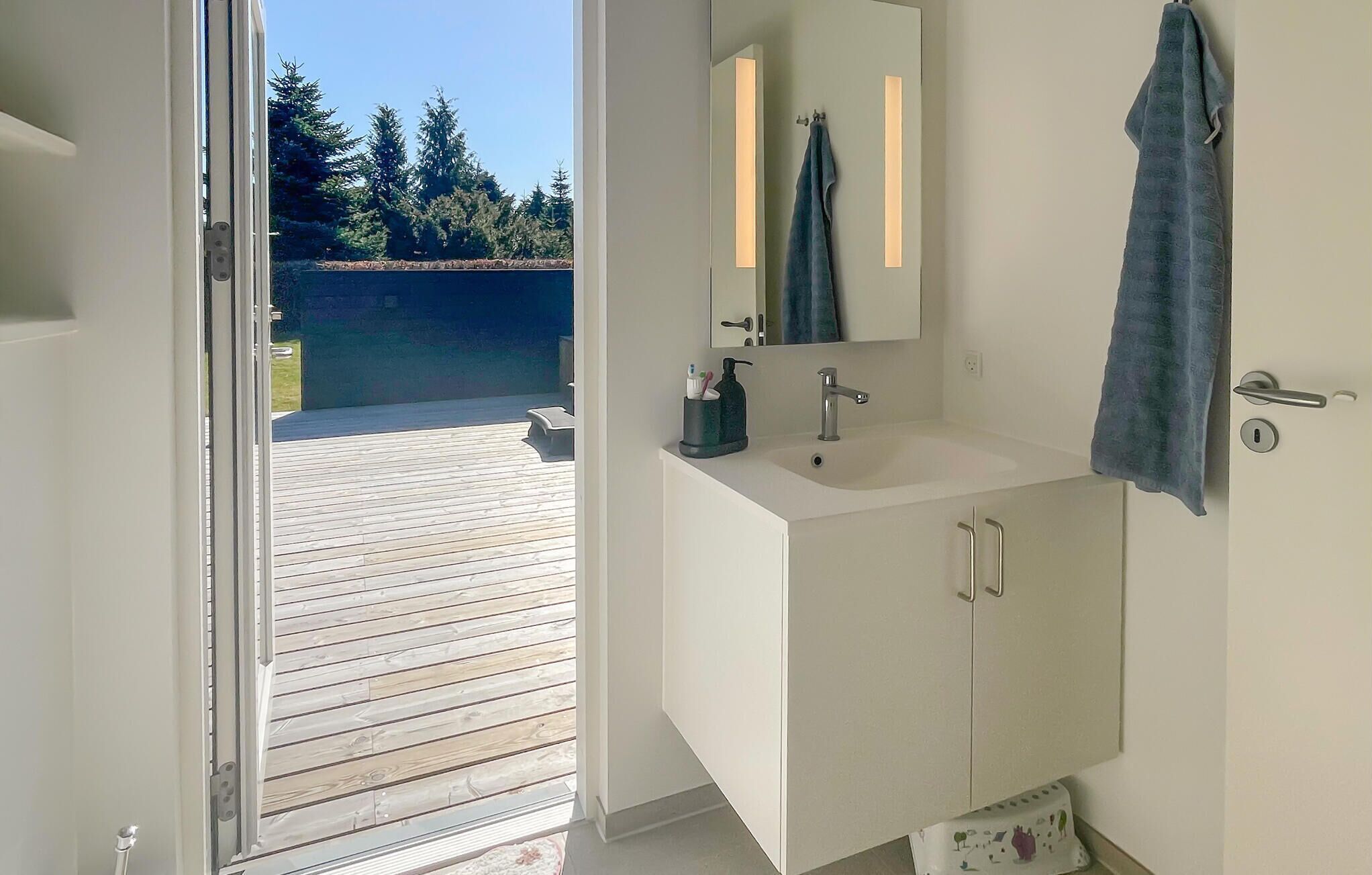 A bathroom with a wooden deck outside, a white sink, a mirror, and a towel hanging on the wall.