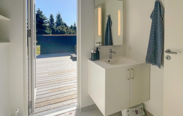 A bathroom with a wooden deck outside, a white sink, a mirror, and a towel hanging on the wall.