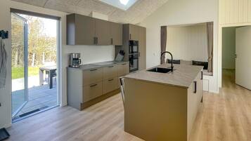 Une cuisine moderne dotée d’un îlot central, d’appareils électroménagers intégrés et d’une porte-fenêtre coulissante donnant sur un espace extérieur.