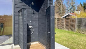 A black wooden outdoor shower with a wooden deck, a metal showerhead, and a hose.