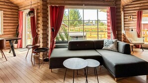 A log cabin interior with a sectional sofa, round tables, and a large window with curtains.