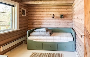 Camera in una baita di legno con un letto, una finestra e una piccola pianta appesa al muro.