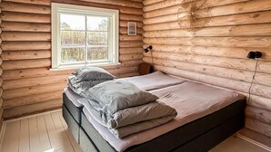 A log cabin bedroom with a bed, pillows, a window, and a wall-mounted light fixture.