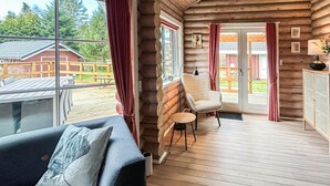 A log cabin interior with a sofa, a chair, a table, and a view of the outside.