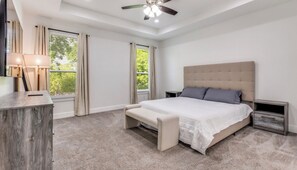 A bedroom with a large bed, a bedside table, a nightstand, a ceiling fan, and a window with curtains. - Spacious 4BR Near Downtown Dallas WiFi + Parking (Dallas)