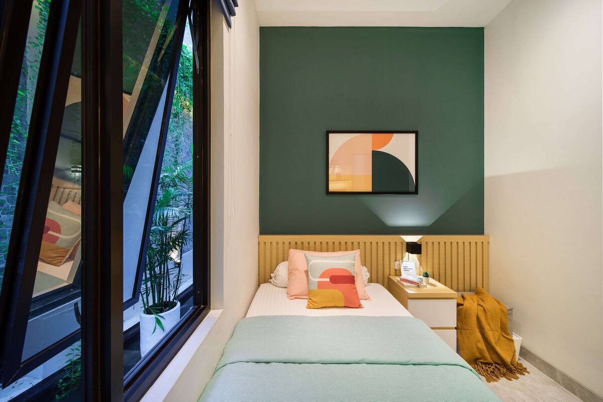 Une chambre à coucher comprenant un lit, une table de chevet, une commode, une fenêtre donnant sur un paysage verdoyant et un tableau abstrait accroché au mur.
