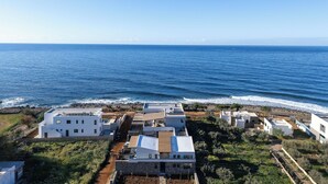 Ein Küstenwohngebiet mit modernen, weißen Gebäuden, freiem Blick auf das Meer und einer unbefestigten Straße, die zum Meer führt.