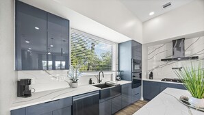 A modern kitchen with dark cabinets, a white countertop, and a window with blinds. - Downtown Hanson- New Constructed 4 level home in East Downtown Houston (Houston)