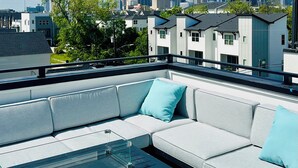 A rooftop terrace with a grey sofa, a glass coffee table, and a city skyline view. - Downtown Hanson- New Constructed 4 level home in East Downtown Houston (Houston)