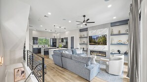 A modern living room with a sectional sofa, a fireplace, and a kitchen in the background. - Downtown Hanson- New Constructed 4 level home in East Downtown Houston (Houston)