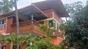 Edifici de dues plantes amb un balcó, envoltat de vegetació.