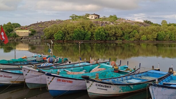 Barques amarrades a una calma massa d'aigua, amb un turó i un edifici petit al fons.