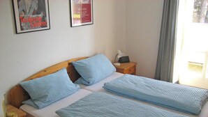 Een tweepersoonsbed met blauw beddengoed, een houten hoofdbord, een nachtkastje met lamp en een ingelijst poster aan de muur.