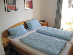 Ein Doppelbett mit blauer Bettwäsche, ein hölzerner Kopfseitenverkleidung, ein Nachttisch mit Lampe und ein gerahmtes Bild an der Wand.