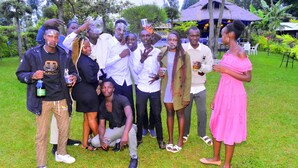 A group of people outdoors, some holding drinks, in a grassy area with trees and a structure in the background. - The Cambrian Village Hotel and Resort (Nyamira)