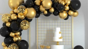 A black and gold balloon arch, a white cake on a pedestal, and gift boxes. - The Cambrian Village Hotel and Resort (Nyamira)
