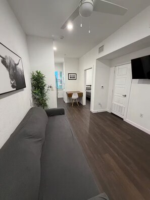 A modern living room with a sofa, a dining table with chairs, a TV mounted on the wall, and a ceiling fan. - Chill 1x1 Apt. in West Campus! (Austin)