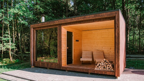 Une cabane en bois moderne dotée d’une porte en verre, d’un banc et d’une cheminée.