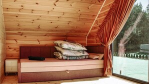 Une pièce chaleureuse aménagée dans un chalet, avec un plafond en bois, un banc rembourré avec des coussins, une petite armoire et une fenêtre avec des rideaux.