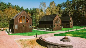 Deux cabanes en bois avec des toits à deux versants, un chemin de gravier et un espace aménagé pour faire un feu de camp.