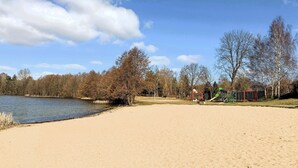 Une plage de sable avec un lac, des arbres et une aire de jeux.